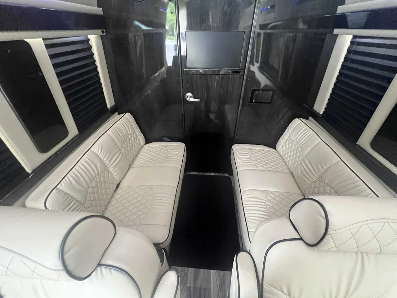 Mercedes Executive Sprinter interior with sofa-style seating, window shades and wood-look flooring for minibus rental