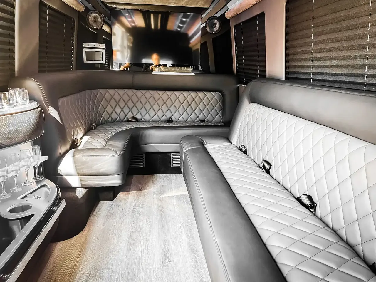 Mercedes-Benz Sprinter Limousine interior with perimeter lounge seating, window shades and wood-look flooring for party bus rental