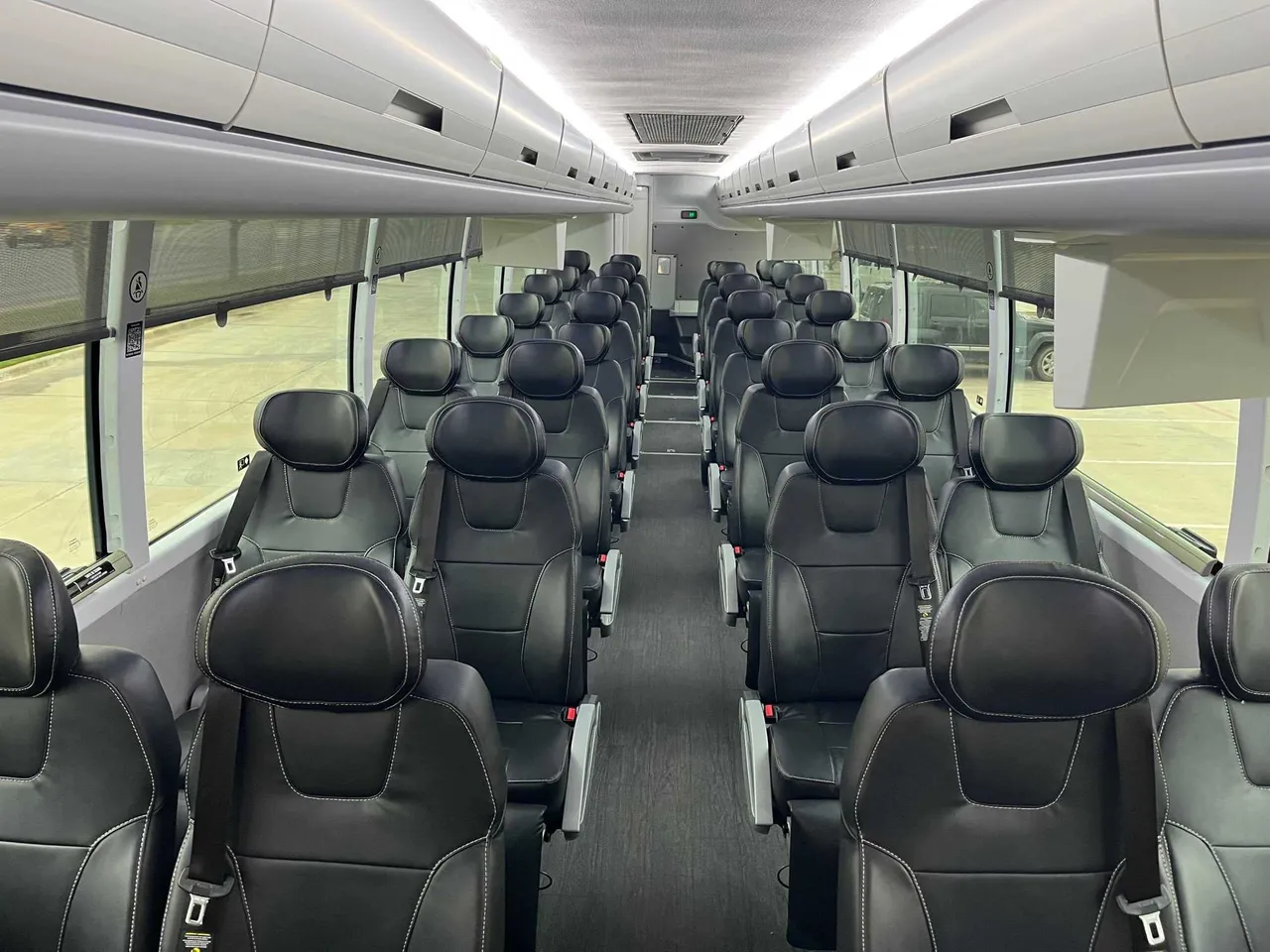 Executive Recliner Motorcoach interior with window shades, LED ceiling lighting and overhead parcel racks for charter bus rental